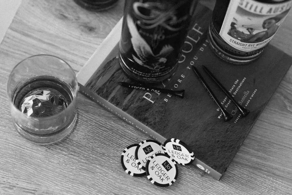 A glass and Ledger & Oak ball markers on a wooden table
